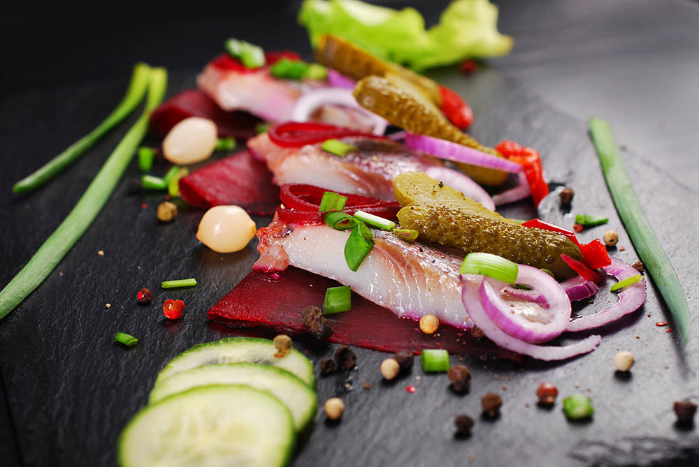 herring appetizer with beets and gherkin on black slate board